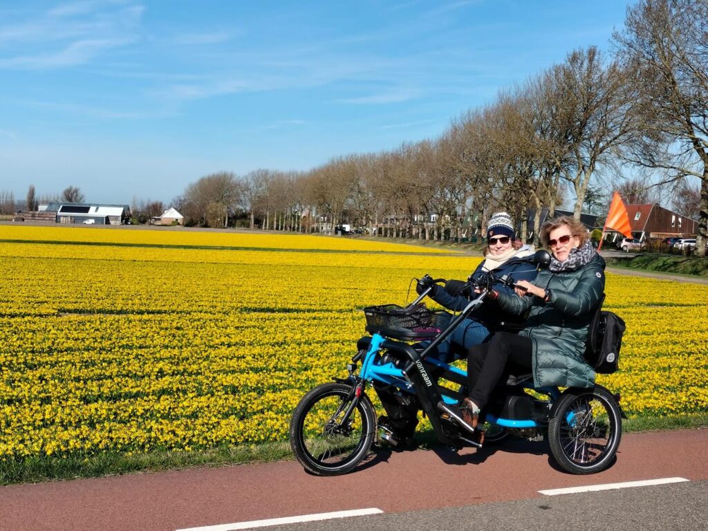 Twee fietsmaatjes op de duofiets bij een prachtig geel bollenveld.